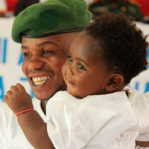 A smiling father holds his child at a Living Peace celebration.