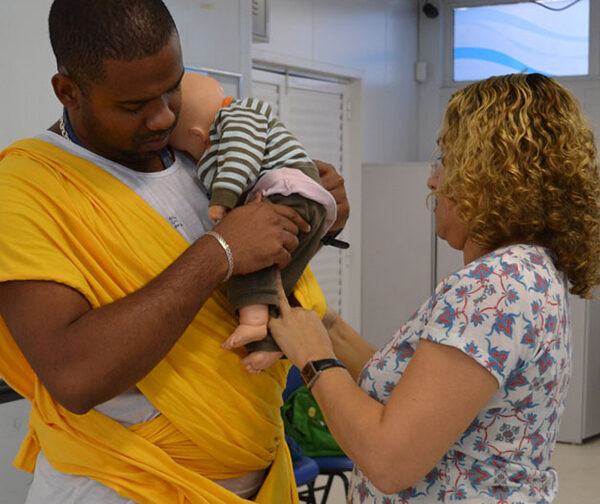 A father learns how to carry a baby in a sling, using a doll, in a MenCare+ workshop in Brazil.