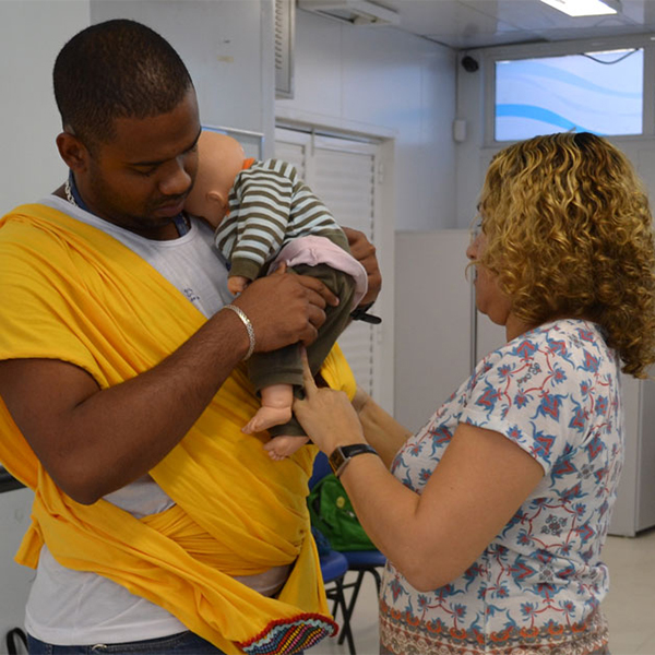 A father learns how to carry a baby in a sling, using a doll, in a MenCare+ workshop in Brazil.