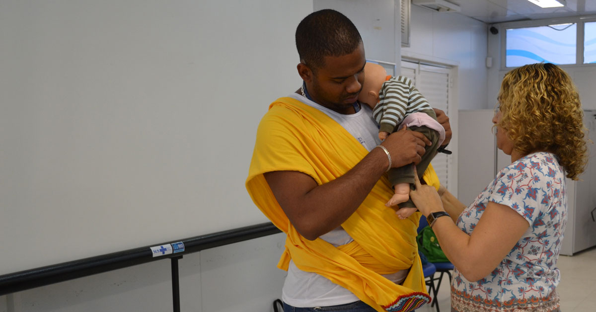 MenCare-Plus-BrazA father learns how to carry a baby in a sling, using a doll, in a MenCare+ workshop in Brazil.